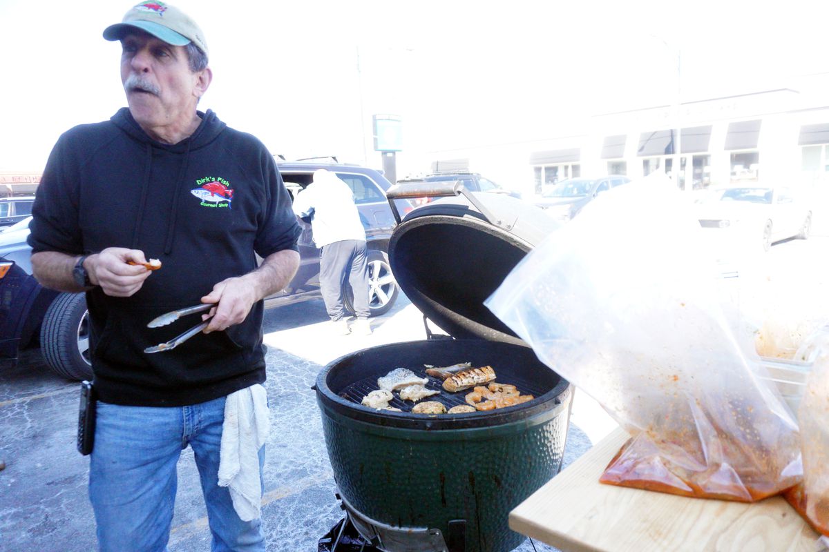A person with tongs grilling fish on a ceramic green grill.