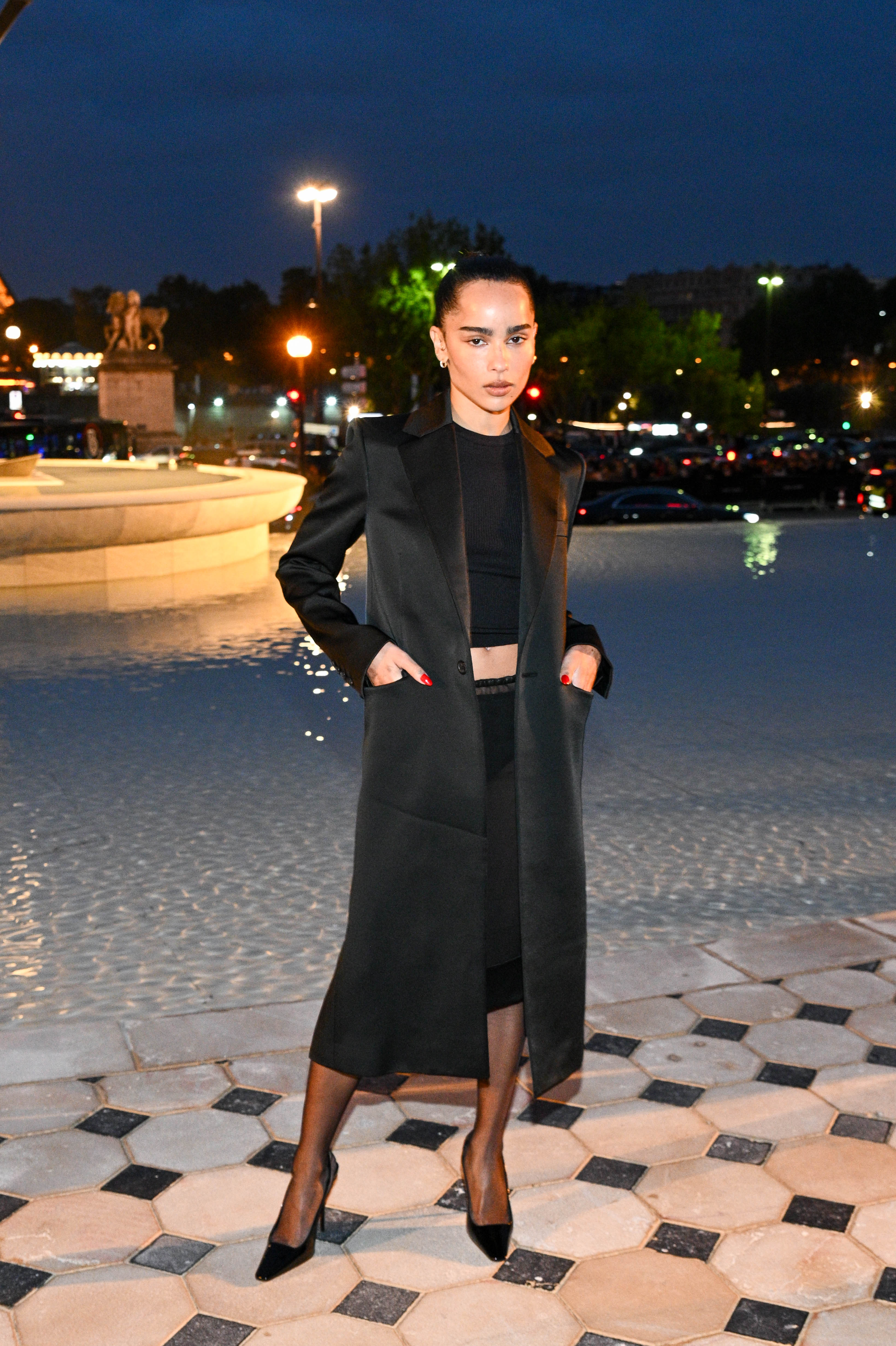Zoe Kravitz mengenakan jubah sutra panjang, kemeja hitam, dan rok pensil hitam. dan sepatu hak tinggi hitam
