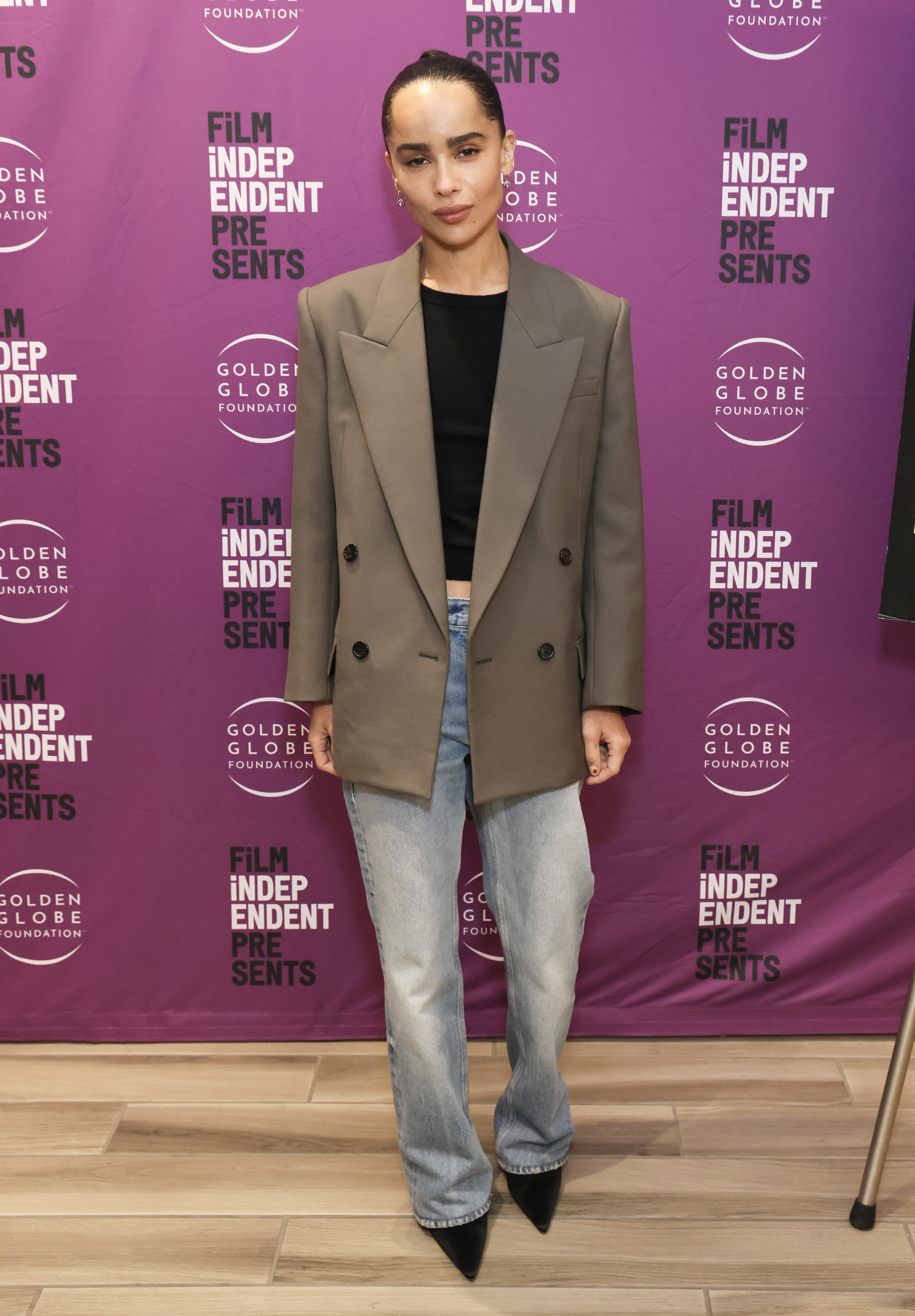 Zoe Kravitz mengenakan blazer coklat, kaos hitam, dan jeans longgar. dan sepatu hak tinggi hitam